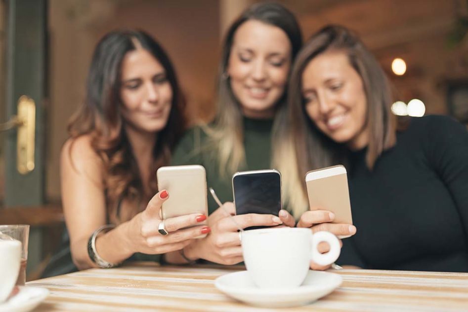 Beautiful friends watching social media in a smart phone in a coffee shop.