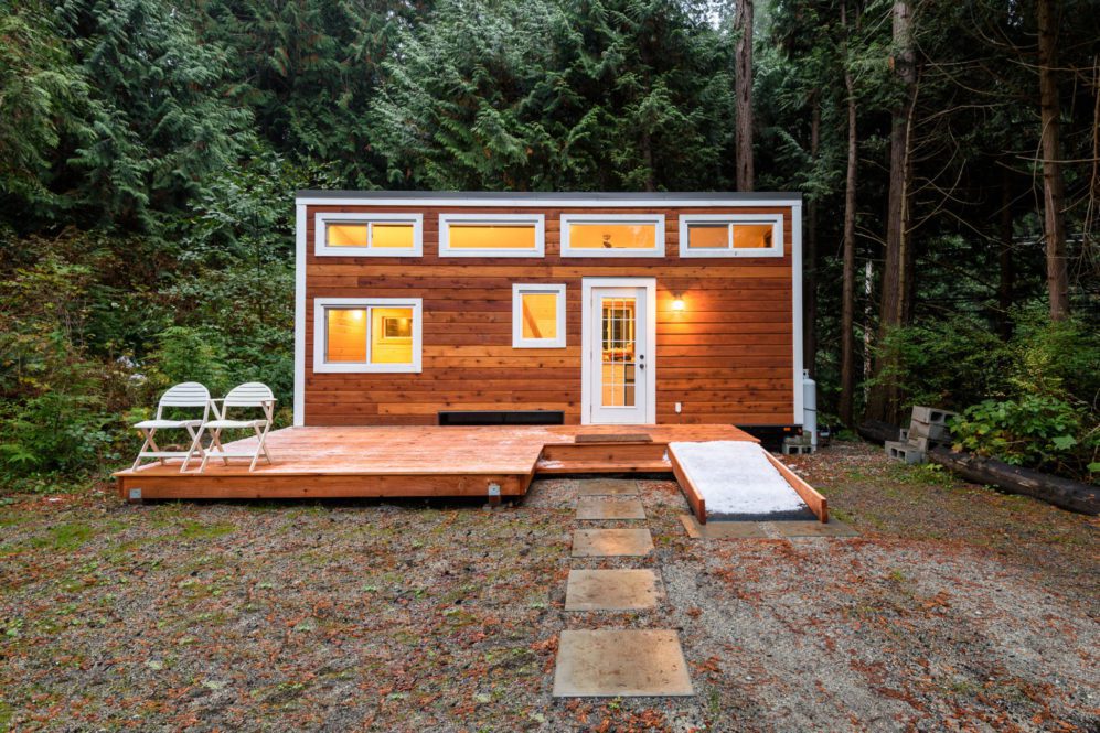 Tiny-house made of wood, set back in the trees with stone walkway.