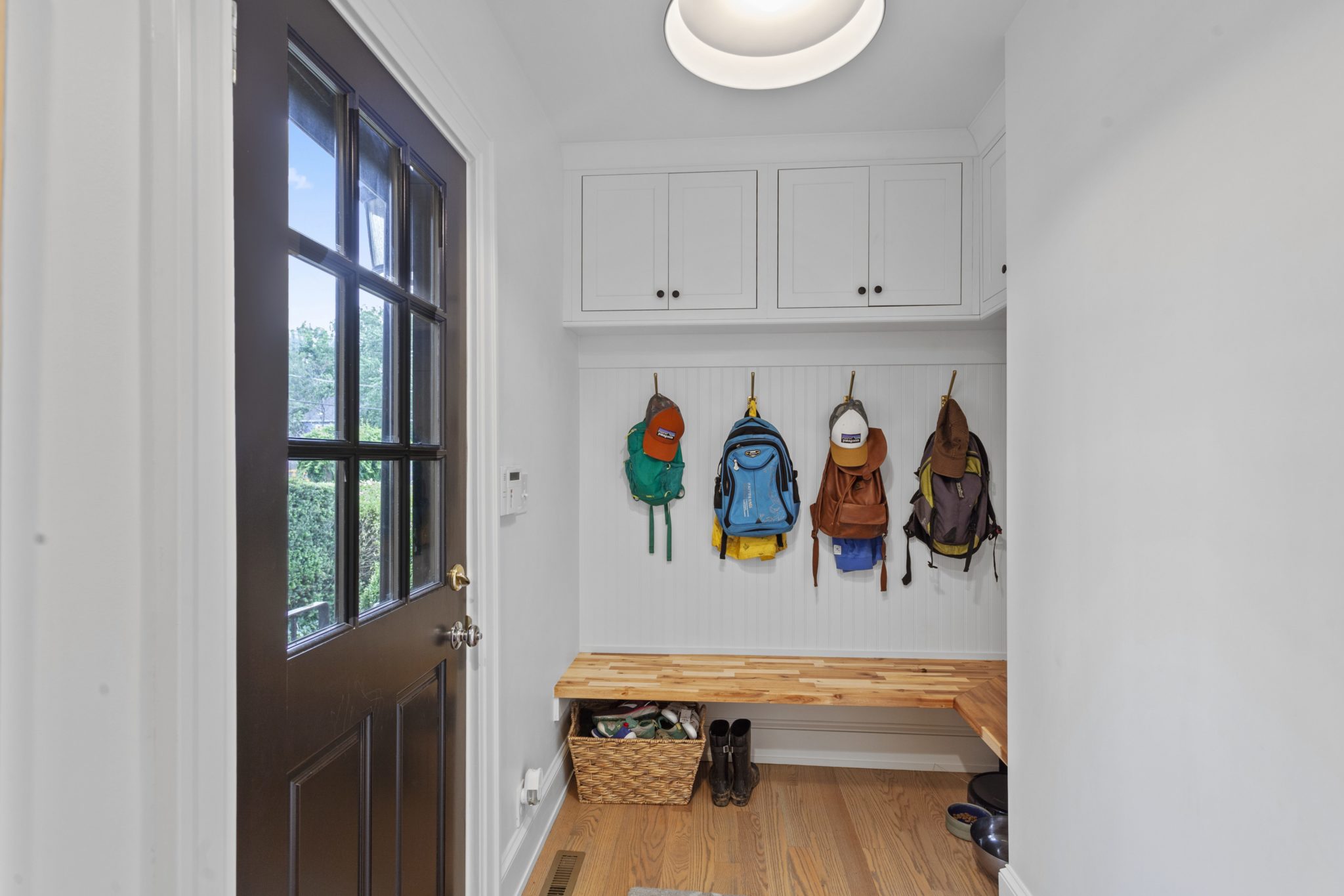 Mudroom with colorful backpacks, hardwood flooring and door to the outside.