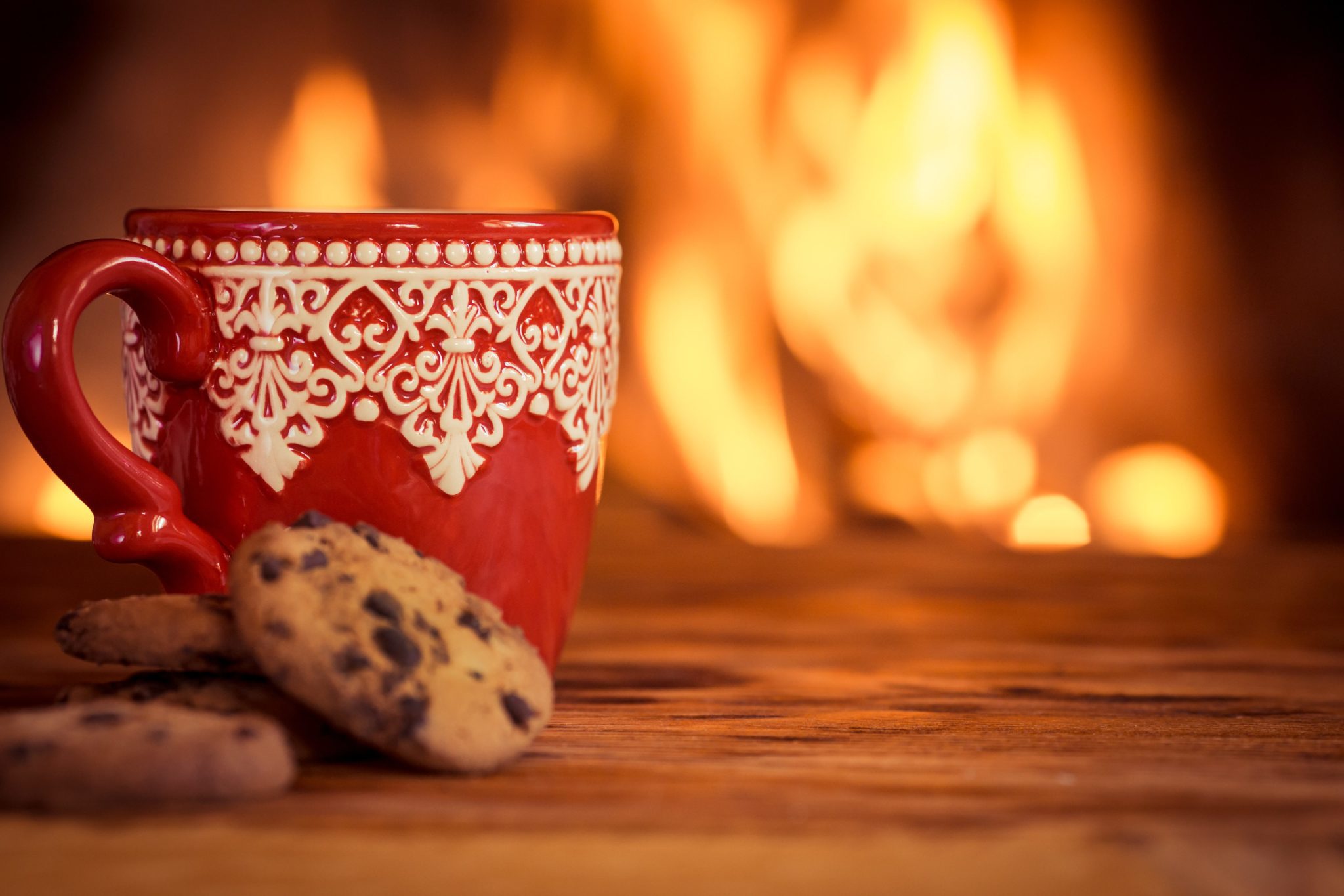 Red and white Christmas mug and chocolate chip cookie near the fireplace.